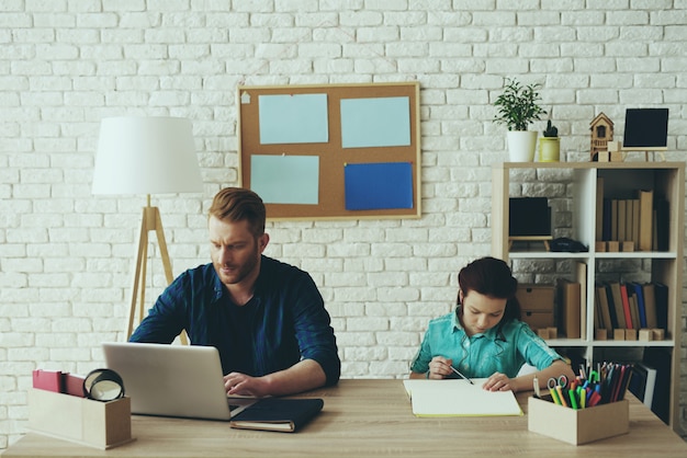 Papá trabaja en la computadora mientras la niña estudia.