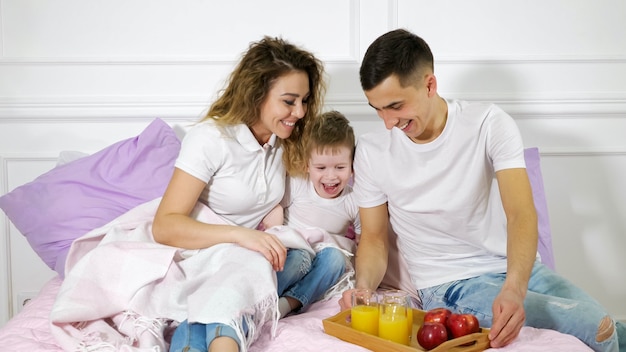 Papá les trajo un bocadillo a mamá e hijo acostados en la cama. Tiempo en familia juntos.