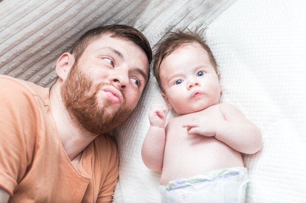 Papa und kleiner Sohn liegen auf dem Bett und verziehen das Gesicht. Nahaufnahmeportrait. Vaterisches Liebeskonzept