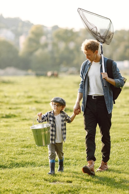 Papa und sein kleiner Junge verbringen gemeinsam Zeit im Freien. Gelockter Kleinkindjunge, der ein kariertes Hemd und einen Hut trägt