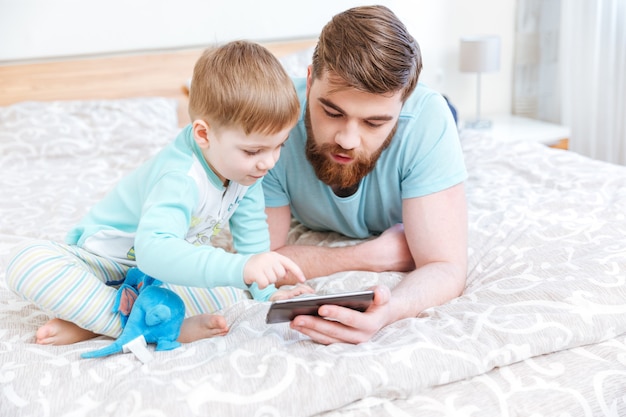 Papa und Sohn liegen im Bett und telefonieren zusammen