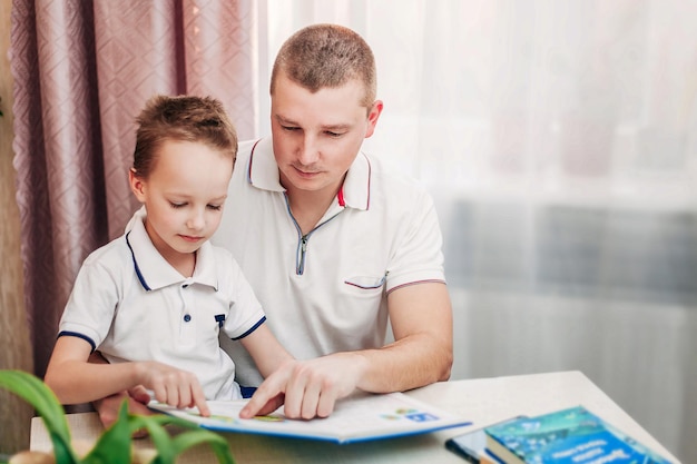 Papa und Sohn sitzen an einem Tisch am Fenster und lesen ein Buch