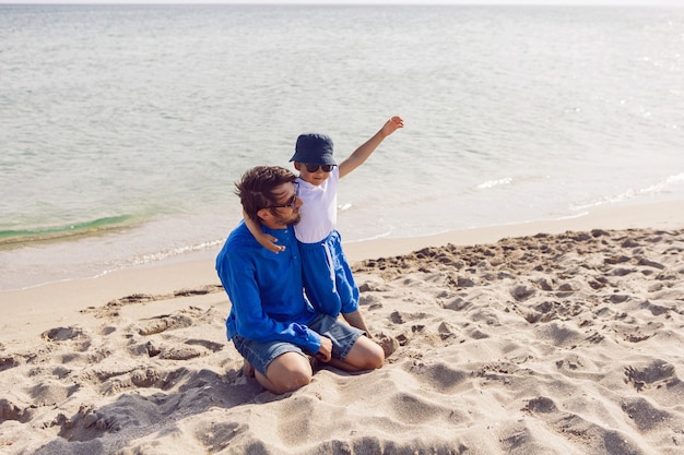 Papa und Sohn spielen im Sommer in blauen Klamotten im Urlaub am Strand