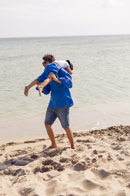 Papa und Sohn spielen im Sommer in blauen Klamotten im Urlaub am Strand