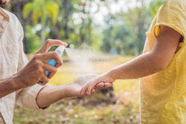 Papa und Sohn verwenden Mückenspray. Insektenschutzmittel auf die Haut im Freien sprühen.