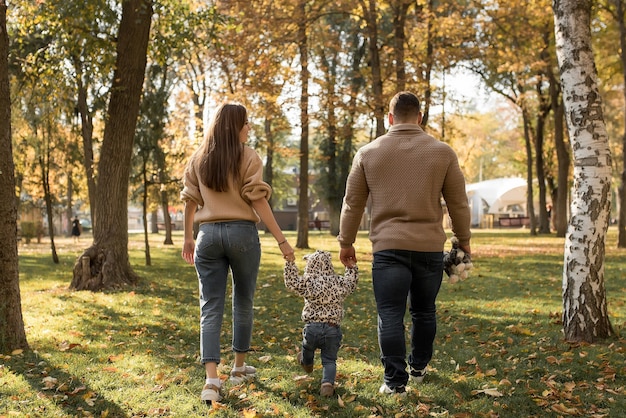 Papai e mamãe estão segurando a mão de suas filhas na floresta de outono