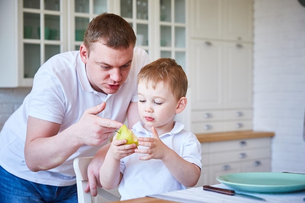 Papai e seu filho estão discutindo uma maçã e comida saudável em uma cozinha espaçosa e brilhante