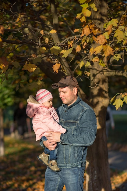 Papai está segurando uma filha de um ano em um bosque de outono