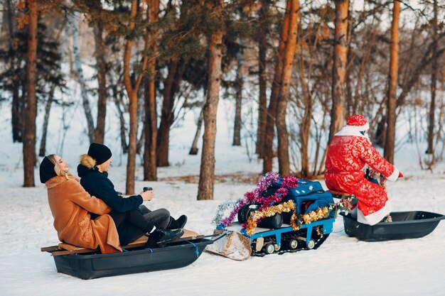 Papai Noel andando de snowmobile casal apaixonado na floresta de inverno