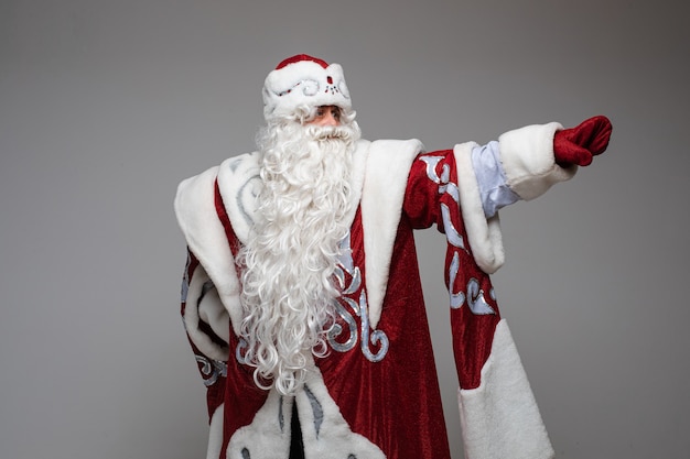 Papai noel apontando com a mão no espaço vazio no fundo cinza do estúdio, com espaço de cópia para publicidade de ano novo de natal. foto de alta qualidade