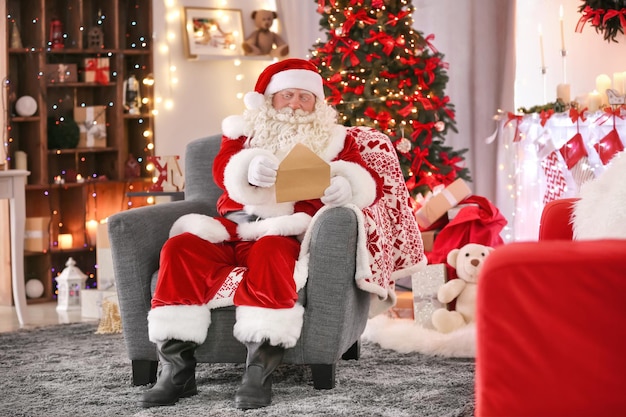 Papai Noel autêntico com carta sentado em uma poltrona em um quarto decorado para o Natal