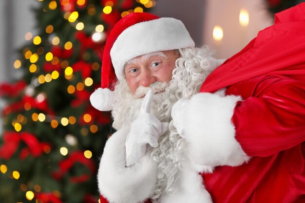 Papai Noel autêntico com uma grande sacola vermelha cheia de presentes contra as luzes de Natal desfocadas