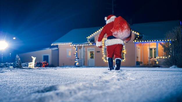 Papai Noel carregando um saco de presentes na frente de uma casa