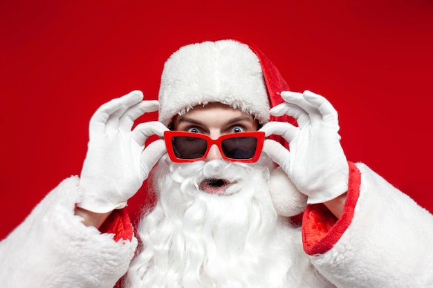 Papai Noel chocado de óculos vermelhos olha para a câmera surpreso e fica surpreso