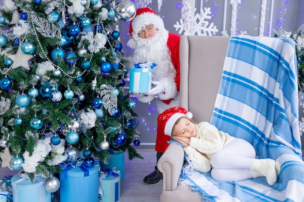 Papai noel coloca um presente debaixo da árvore enquanto a criança está dormindo