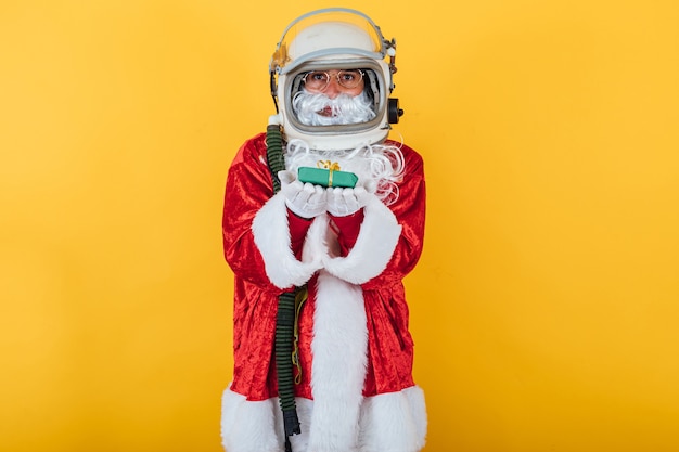 Papai Noel com capacete de astronauta segurando um presente em amarelo