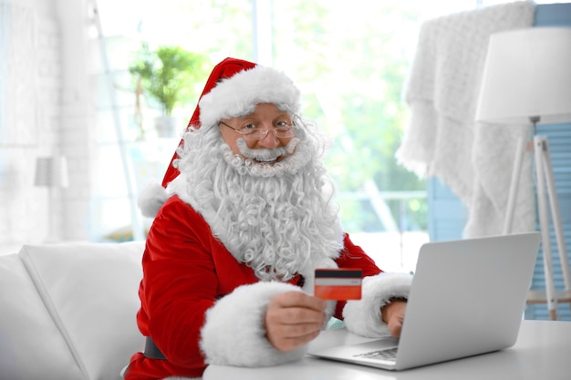 Papai Noel com cartão de crédito e laptop em casa