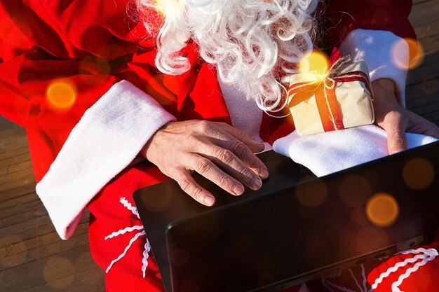 Papai noel com um laptop e um presente na mão. encomende presentes para o natal e ano novo através da loja online. reservar os serviços de um animador para as férias.