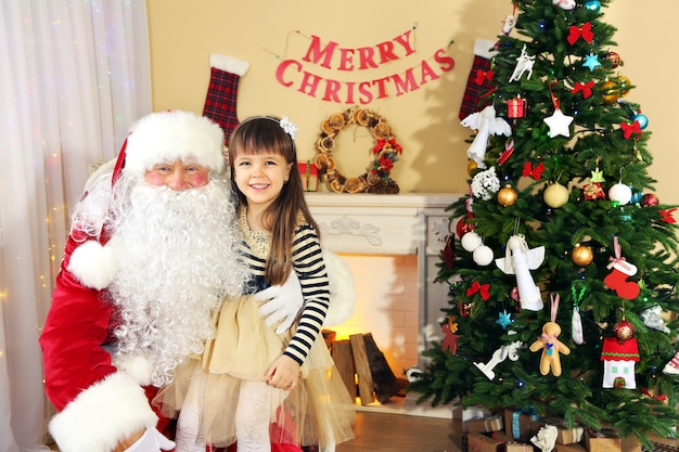 Papai Noel com uma linda garotinha perto da árvore de Natal em casa