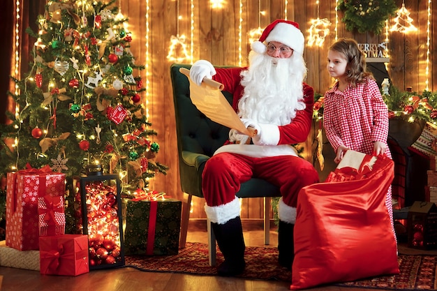 Papai noel com uma linda menina espantada em pijama embalar presentes