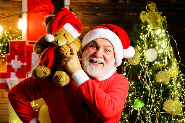 Papai noel com ursinho de pelúcia nos ombros feriados de natal homem barbudo em fantasia de papai noel perto