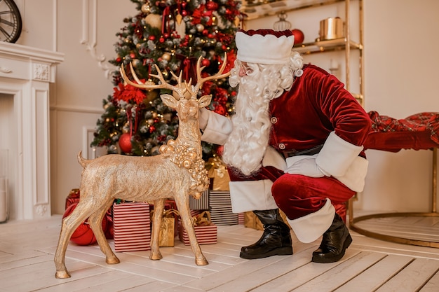 Papai Noel e veados perto da lareira e árvore de Natal com presentes. Ano novo e feliz natal, conceito de boas festas