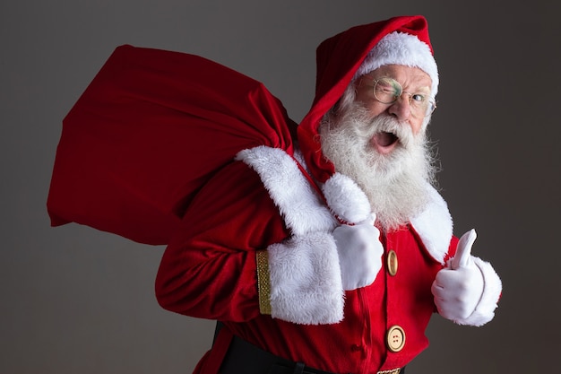 Papai Noel em óculos está olhando para a câmera e sorrindo, em um fundo cinza