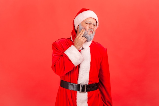 Papai Noel em pé e tocando sua bochecha, sofrendo de uma terrível dor de dente.