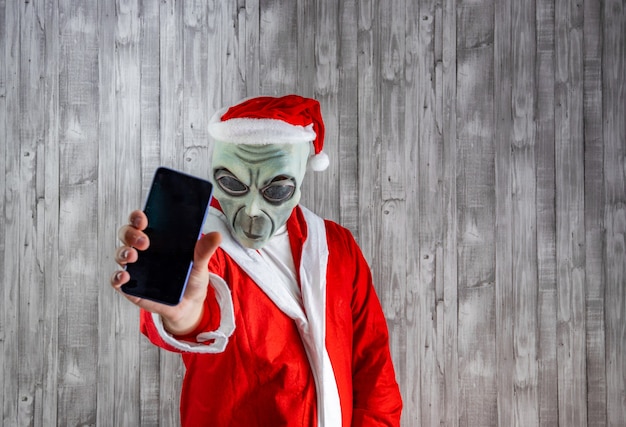Papai Noel fantasiado de alienígena mostrando o celular em primeiro plano