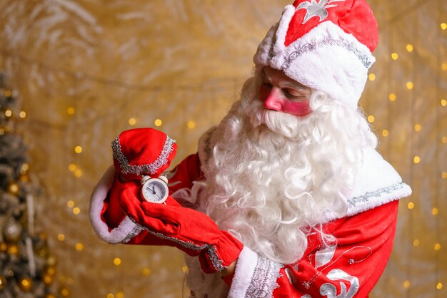 Papai Noel feliz segura um despertador e assina no fundo da árvore de Natal esperando o n ...