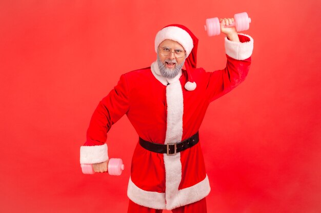 Papai Noel levantou os braços com halteres rosa, olhando para a câmera, mostrando seu poder, parece orgulhoso.