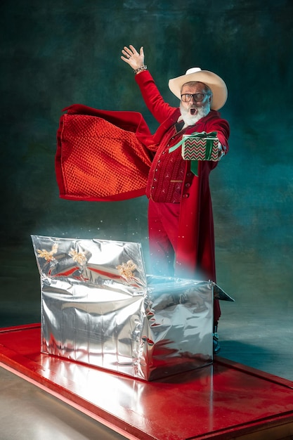 Papai Noel moderno e elegante em um terno vermelho elegante e chapéu de cowboy em fundo escuro