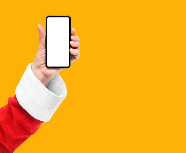 Foto papai noel mostra o telefone inteligente com tela em branco isolada em fundo amarelo laranja