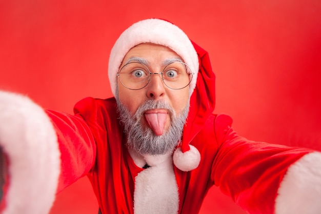 Foto papai noel mostrando a língua ao fazer selfie foto de ponto de vista, emoções positivas.