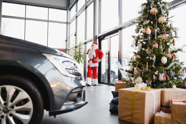 Papai noel perto de um carro novo em uma concessionária de automóveis.