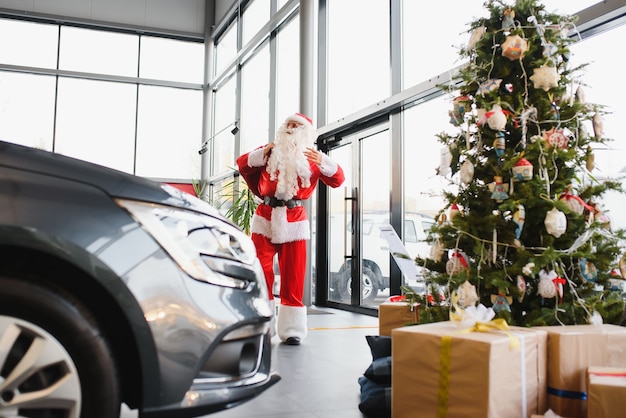 Papai noel perto de um carro novo em uma concessionária de automóveis.