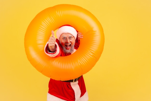 Papai Noel posando com anel de borracha laranja e aparecendo o polegar, aproveitando as férias de inverno.