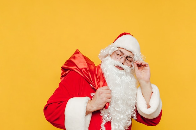 Papai Noel preocupado está tocando seus óculos de proteção e olhando para seu saco vermelho com presentes