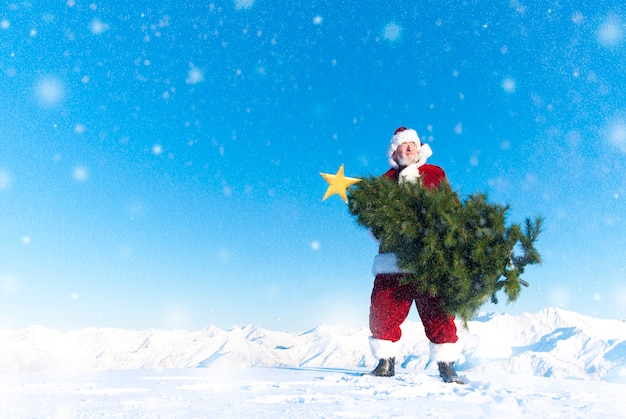 Papai Noel que leva uma árvore de Natal em uma montanha coberto de neve.