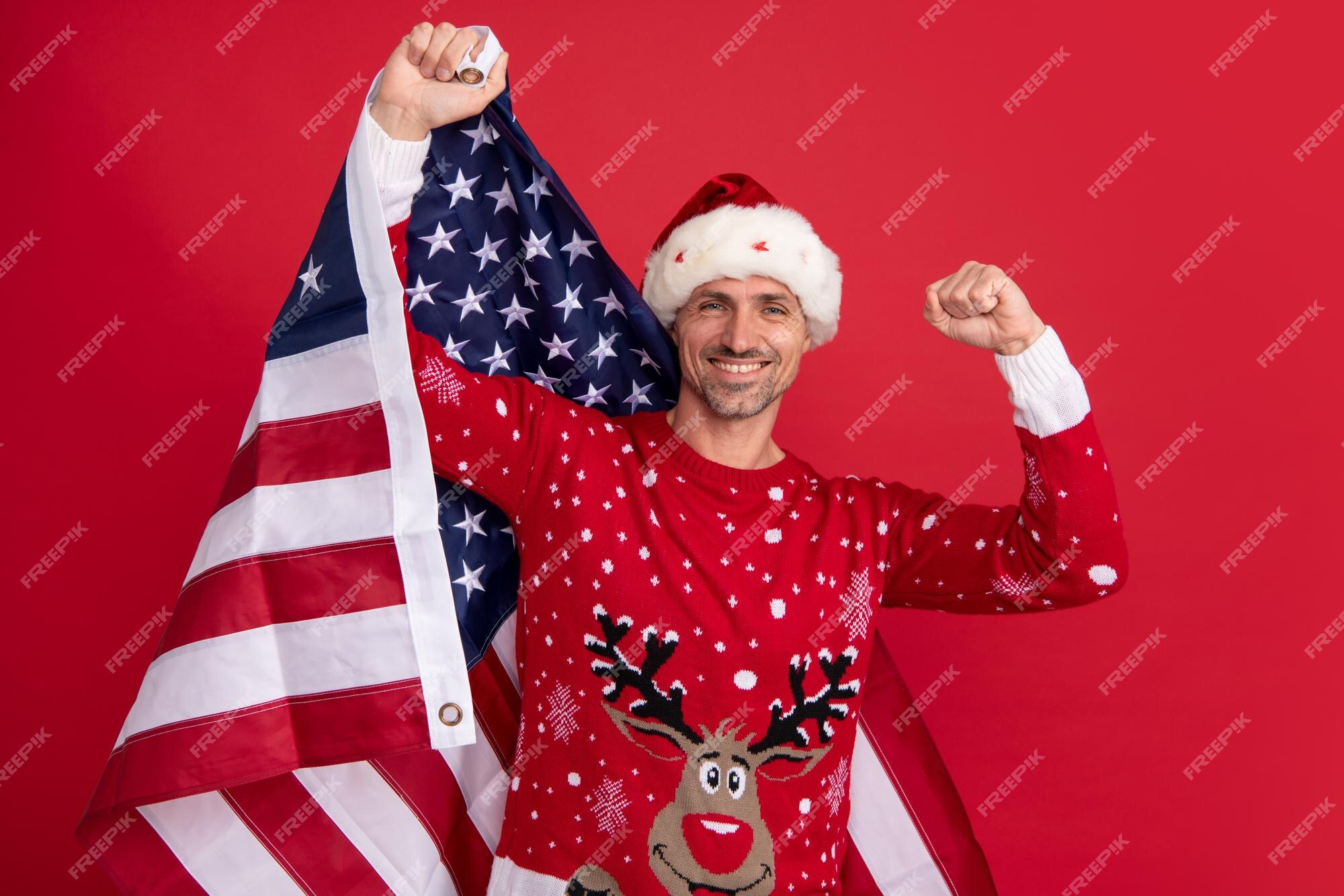 Papai noel segura a bandeira americana natal nos estados unidos eua retrato de um homem de meia idade em um suéter isolado sobre fundo vermelho conceito de emoções de felicidade de feriados Papai noel segura a bandeira americana natal nos estados unidos eua retrato de um homem de meia idade em um suéter isolado sobre fundo vermelho conceito de emoções de felicidade de feriados
