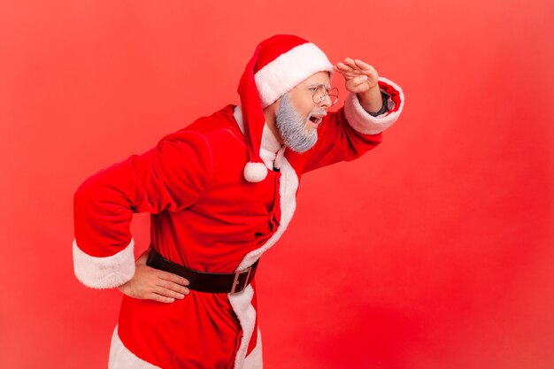 Papai Noel segurando a mão acima dos olhos e olhando para longe, olhando para longe, procurando alguém.