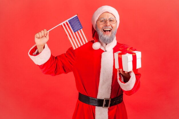 Papai Noel segurando nas mãos a bandeira dos EUA, dando caixa de presente para férias de inverno.