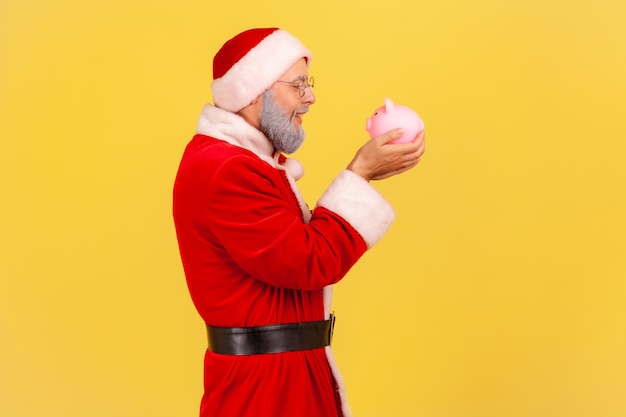 Papai Noel segurando o cofrinho nas mãos, feliz com a poupança.