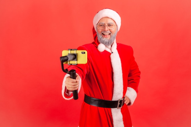 Papai Noel segurando Steadicam, transmitindo transmissão ao vivo, blogueiro conversando com seguidores.