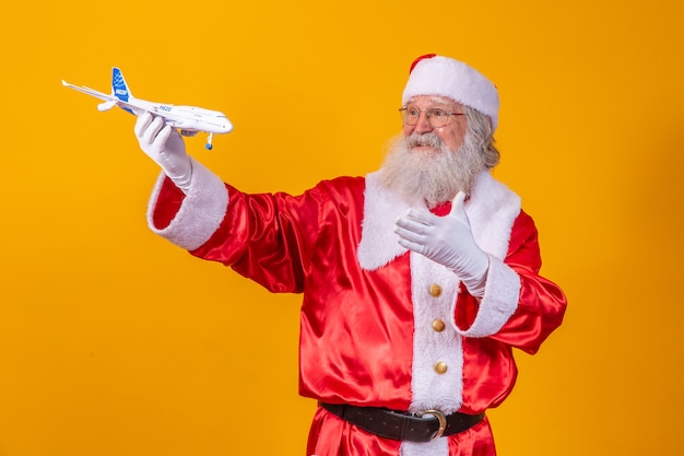 Papai Noel segurando um pequeno avião de brinquedo em fundo amarelo. Conceito de viagem de natal