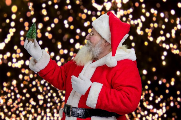 Papai Noel segurando uma árvore de Natal decorativa.