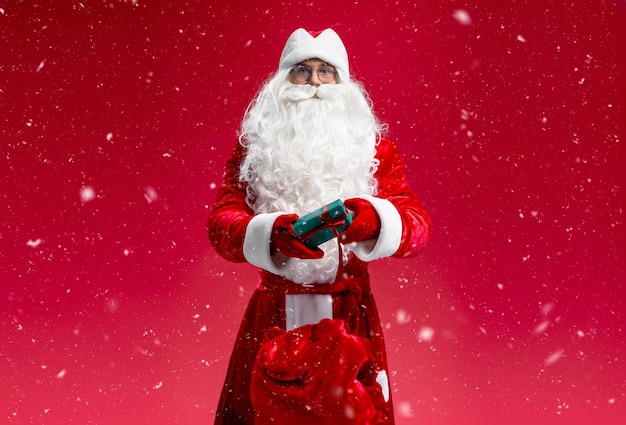 Papai Noel segurando uma caixa de presentes olhando para a câmera isolada em fundo vermelho