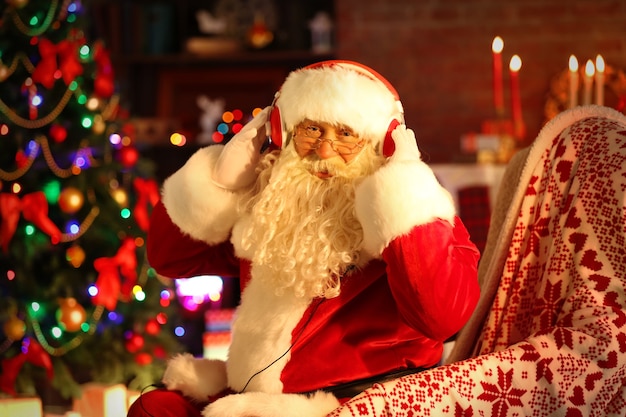 Papai Noel sentado com fones de ouvido sentado em uma cadeira de balanço confortável em casa