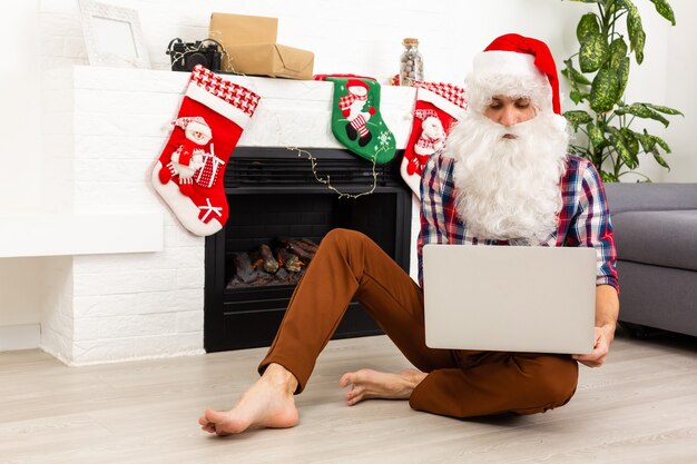 Papai Noel sentado com um laptop no fundo da lareira