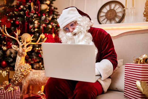 Papai Noel sentado em casa lendo e-mail no laptop